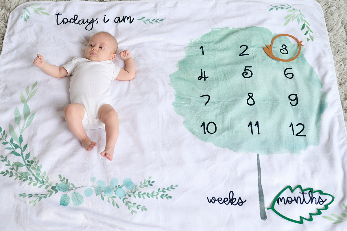 3 month old infant lying on a milestone blanket.